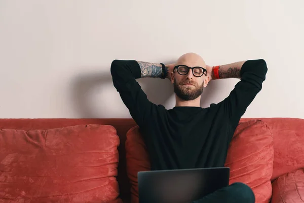 Modern man sitting on couch with laptop relaxing with hands behind head — Stock Photo, Image