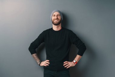 Gri stüdyo arka planında sakallı, gülümseyen genç adam.