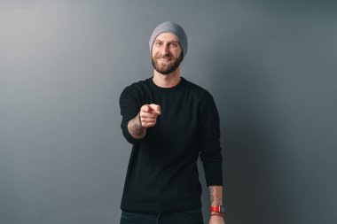 Gri stüdyo arka planında sakallı, gülümseyen genç adam.