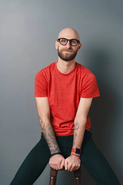 Молодой улыбающийся человек с бородой и в очках на сером фоне студии — стоковое фото