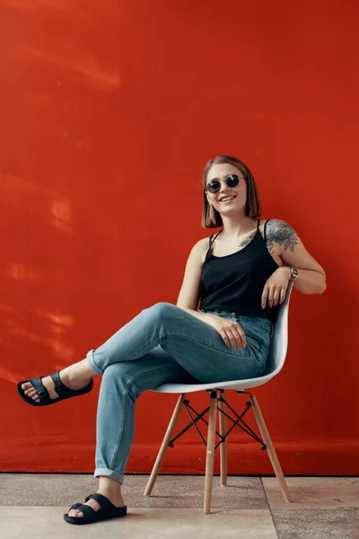 Jeune fille assise sur une chaise blanche près du mur rouge — Photo