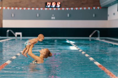Anne ve küçük oğlu yüzme havuzunda eğleniyor.