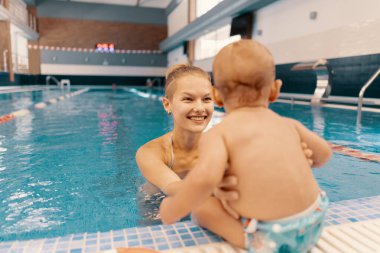 Anne ve küçük oğlu yüzme havuzunda eğleniyor.
