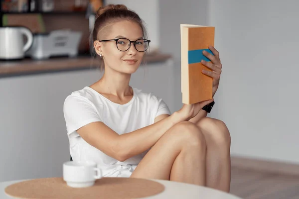 Ragazza carina sta bevendo caffè e leggendo un libro — Foto Stock