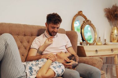 Oturma odasındaki kanepede sevgi dolu bir çift. Kız adamın kucağında yatıyor.