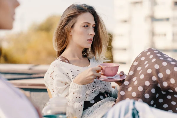 Two attractive girls enjoy a tea party on the rooftop overlooking the city. Drinking healthy buckwheat tea. Healthcare or herbal medicine concept.