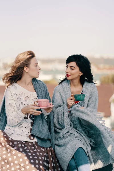 Two attractive girls enjoy a tea party on the rooftop overlooking the city. Drinking healthy buckwheat tea. Healthcare or herbal medicine concept.