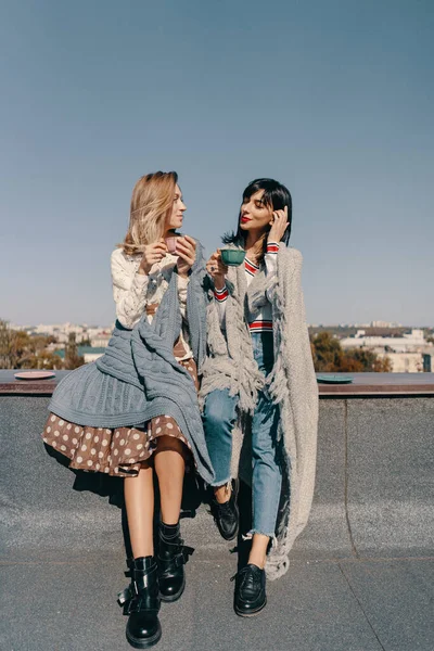 Two attractive girls enjoy a tea party on the rooftop overlooking the city. Drinking healthy buckwheat tea. Healthcare or herbal medicine concept.