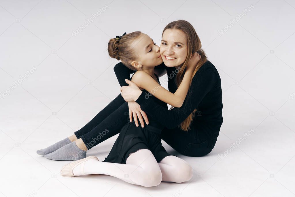Mother encourages her daughter ballerina sitting on the floor on white background.