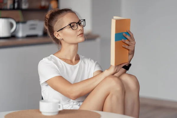 Menina bonito está bebendo café e lendo um livro — Fotografia de Stock