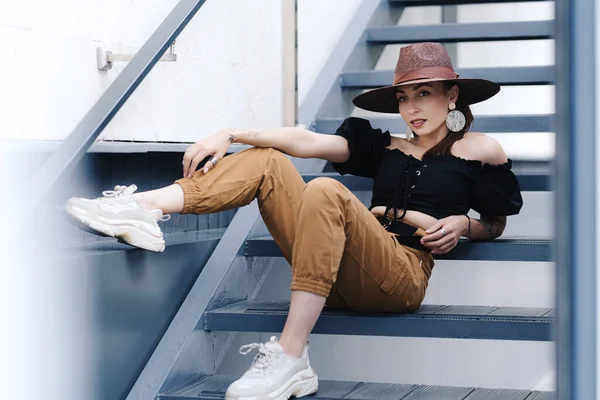 Modieuze brunette vrouw met lang haar, dragen stijlvolle grote rieten hoed, poseren op de trap — Stockfoto