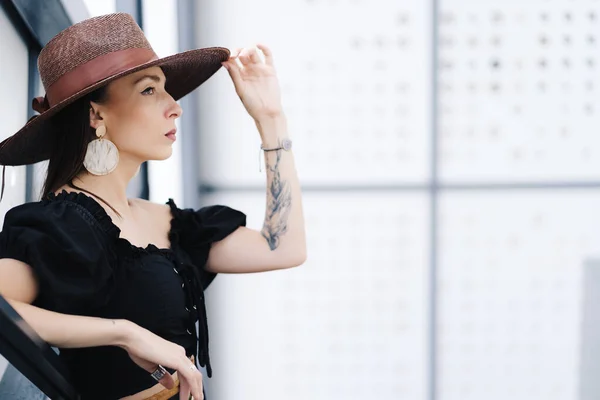 Modische brünette Frau mit langen Haaren, trägt stylische große Korbmütze, posiert auf der Treppe — Stockfoto