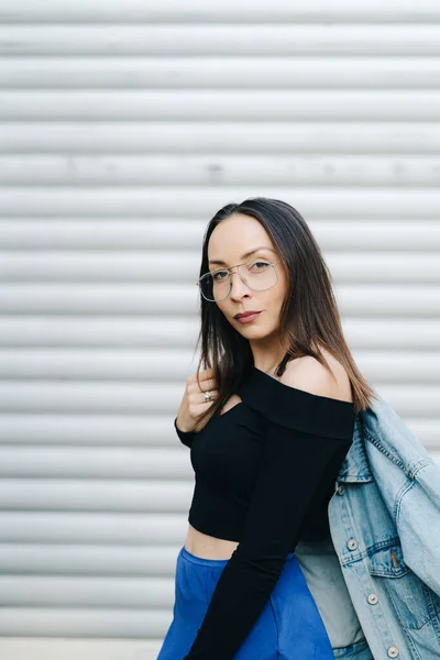 Retrato de mujer joven con gafas. Mujer de estilo bonito con el pelo largo y oscuro con una chaqueta de mezclilla — Foto de Stock