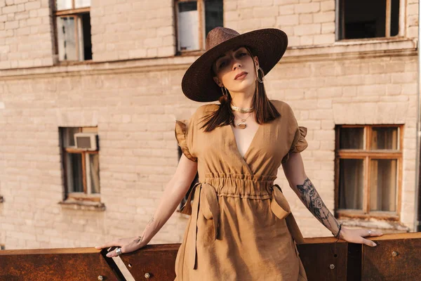 Menina de moda jovem vestida em um vestido de verão com um chapéu largo de vime caminha e posa na cidade velha — Fotografia de Stock