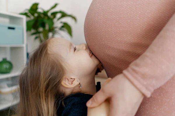 Беременная женщина и ее маленькая дочь целуют ее живот — стоковое фото