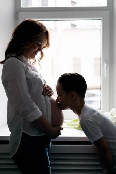 Eine schwangere Frau und ihre Vorschulsonne küssen ihren Bauch — Stockfoto