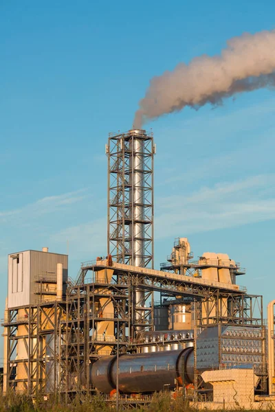Industrial plant with smoke exhaust out of a pipe on a blue sky background
