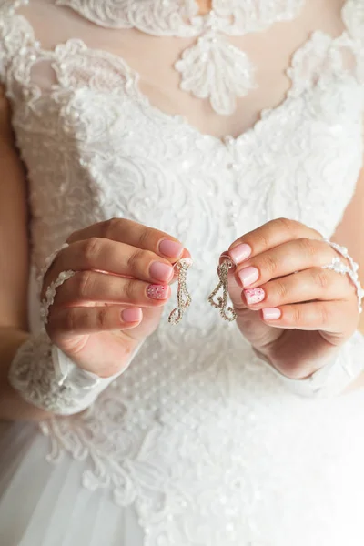 Vackra eleganta örhängen i händerna på bruden — Stockfoto