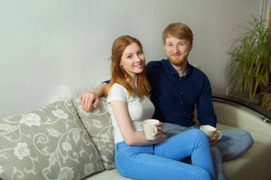 güzel genç çift adam ve kız kanepede oturan ve çay içme Kızıl saçlı