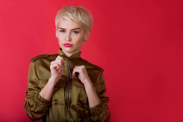 beautiful stylish young girl with a short hairstyle on a red background with a serious facial expression