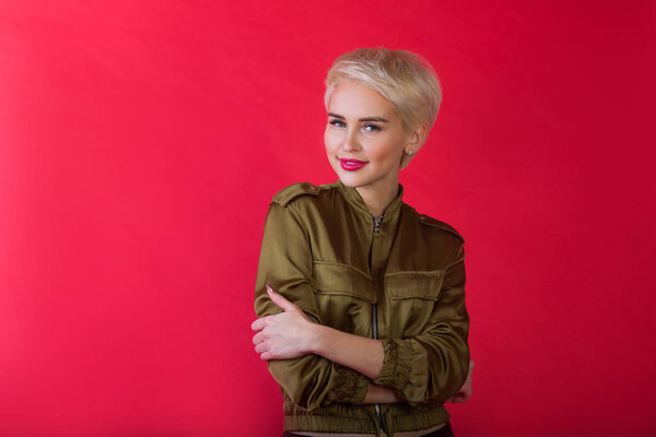 beautiful young girl with a smile and with a short hairdo in a jacket on a red background