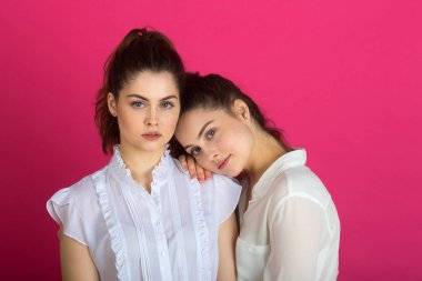 iki güzel genç kız ikiz sakin ve üzgün bir ifade ile pembe bir arka plan üzerinde beyaz bluz