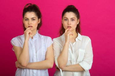 iki güzel genç kız iyi bir ruh hali içinde pembe bir arka plan üzerinde beyaz bluz dalgın bir ifade ile ikiz.