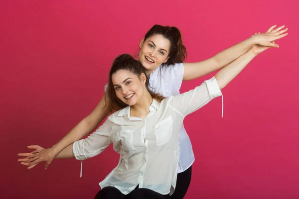 两个美丽快乐的年轻女孩姐妹在粉红色的背景手势与表情的脸 — 图库照片