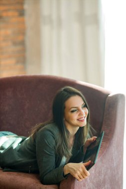 güzel genç kız siyah saçlı bir tablet ellerde ile kanepede yalan