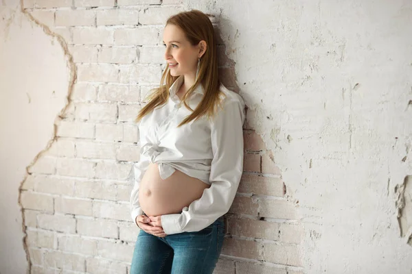 Piękna Młoda Dziewczyna Ciąży Białej Koszuli Dżinsy Stojąc Pobliżu Ściany — Zdjęcie stockowe