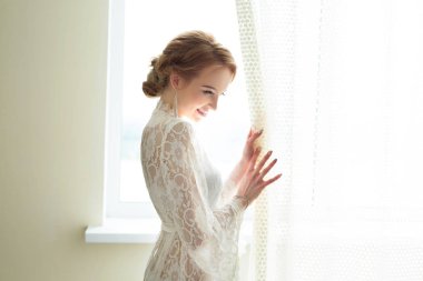 Beyaz dantel soyunma ayakta pencere yakınındaki güzel genç gelin