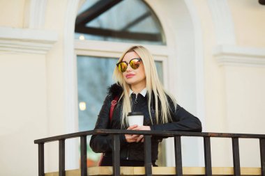 güzel genç kız bir siyah ceket ve elinde kahve bir fincan ile sokakta gözlük