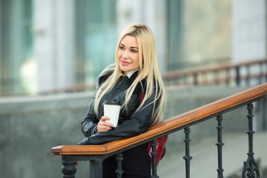 bir fincan kahve elinde siyah bir ceketle açık havada güzel genç kız