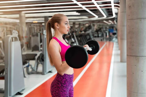 beautiful young girl in a sport suit at the gym with a barbell in hands