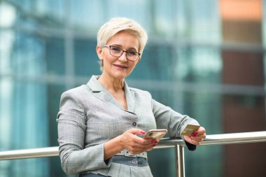 Kısa saçlı, takım elbiseli, elinde telefon ve kredi kartıyla şık bir kadın.