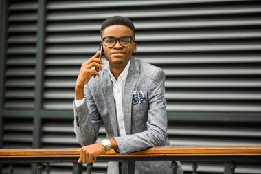 Takım elbiseli, gözlüklü yakışıklı Afrikalı bir adam telefonda.