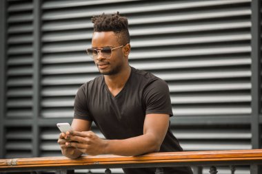 Siyah tişörtlü, gözlüklü, elinde telefon olan yakışıklı bir Afrikalı.