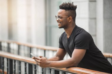 Siyah tişörtlü, gözlüklü, elinde telefon olan yakışıklı bir Afrikalı.