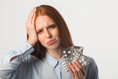 Güzel bir genç kadın, kızıl saçlı, elinde haplarla beyaz bir arka planda.