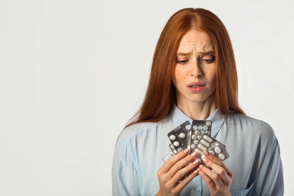 beautiful young woman with red hair with pills in hands on a white background