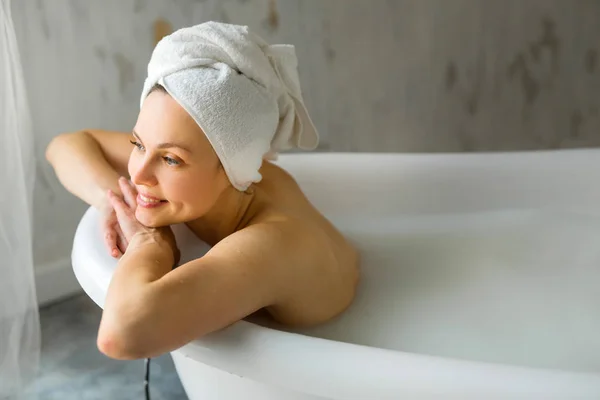 Kafasında havluyla küvette sütle yıkanan güzel bir genç kadın.