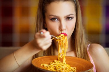 Makyajlı genç bir kadın restoranda spagetti yiyor.