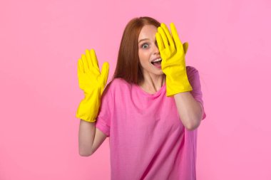 Pembe arka planda sarı lastik eldivenli kızıl saçlı güzel bir genç kadın.