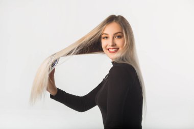 Beyaz arka planda uzun saçlı güzel genç bir kadın saçını tarıyor.