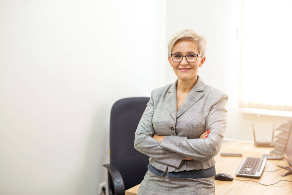 взрослая женщина в костюме и очках за столом в помещении
