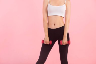 Pembe arka planda, ellerinde dambıllar olan ince, genç bir kadın.