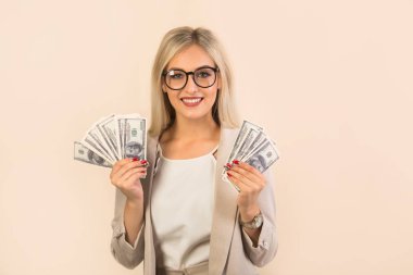 Bej arka planda takım elbiseli güzel genç bir kadın. Elinde dolarlarla.
