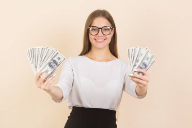 Bej arka planda gözlüklü genç bir kadın, ellerinde dolarlarla.