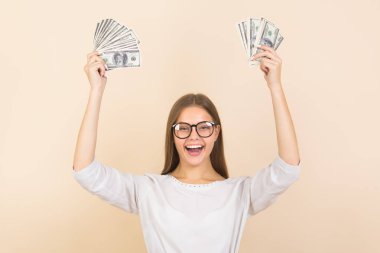 Bej arka planda gözlüklü genç bir kadın, ellerinde dolarlarla.