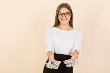 Bej arka planda gözlüklü genç bir kadın, ellerinde dolarlarla.